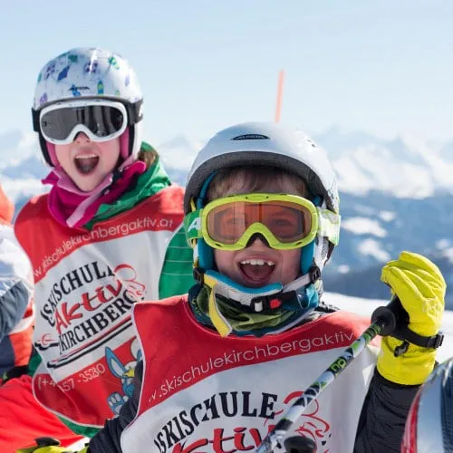 Kinder in Skischule mit Skihelmen und Brillen auf einer Piste