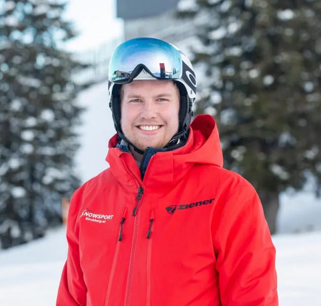 Lächelnder Ski-Guide in roter Jacke, Schnee im Hintergrund