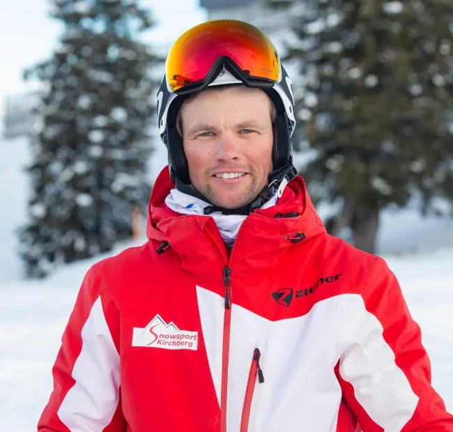 Skilehrer in roter Jacke vor verschneitem Hintergrund