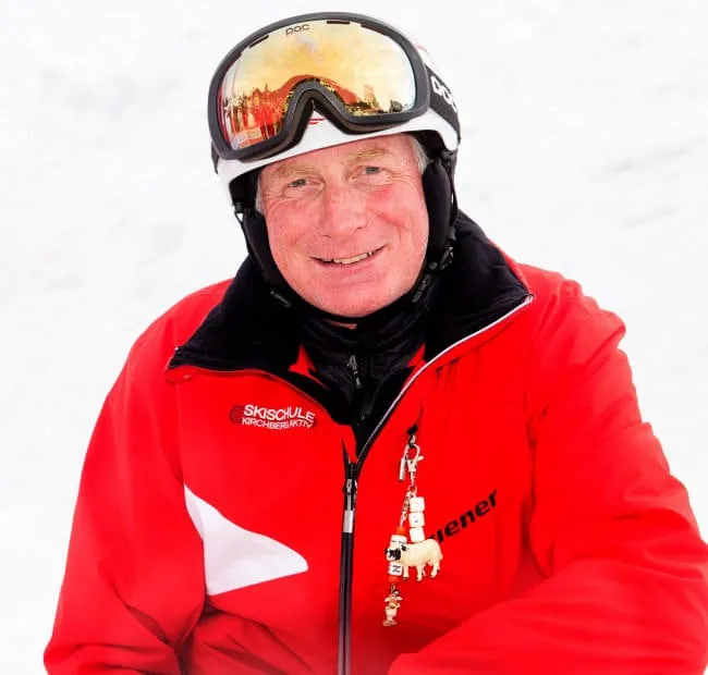 Lächelnder Mann in roter Ski-Jacke vor schneebedecktem Hintergrund