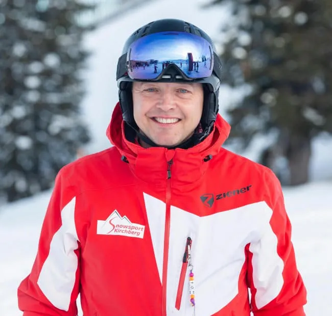 Lächelnder Skifahrer in roter Jacke an schneereichem Ort