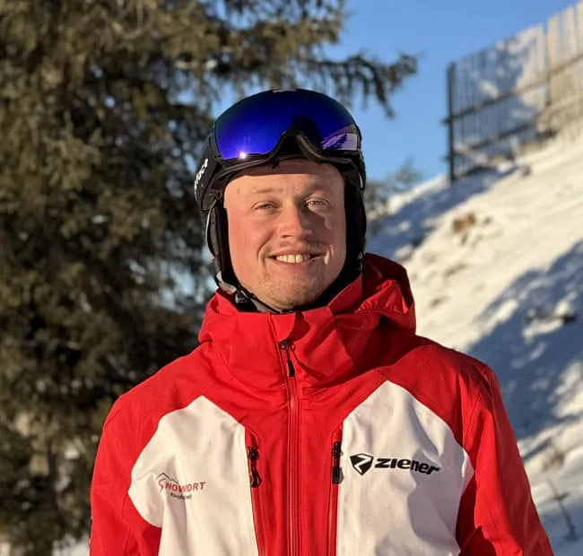 Skifahrer in roter Jacke mit Fichten im Hintergrund