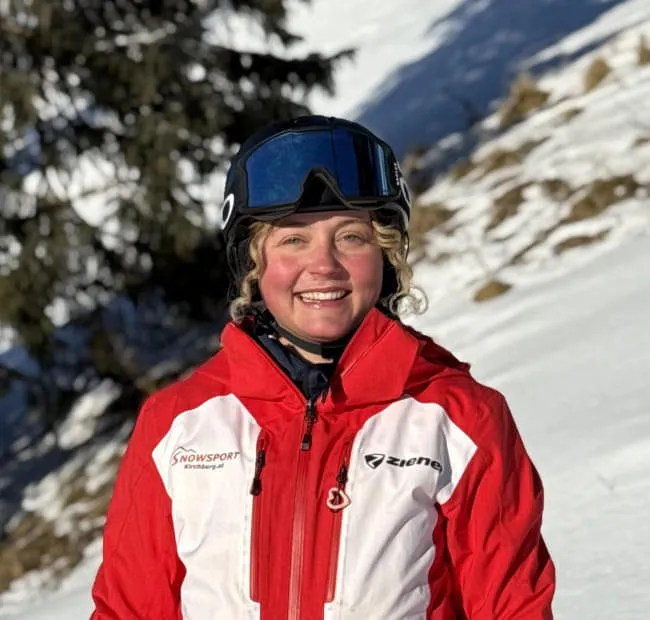 Lächelnde Skifahrerin in roter Jacke auf Schneehügel