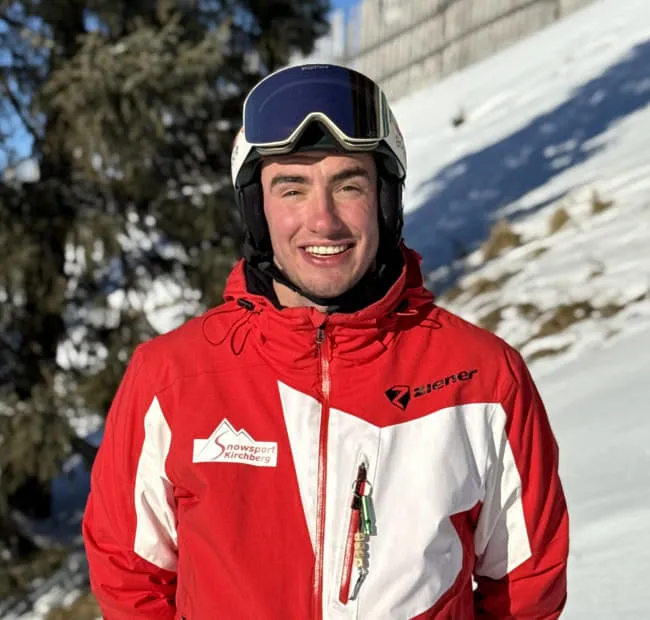 Junger Skifahrer im roten Outfit vor verschneitem Hintergrund