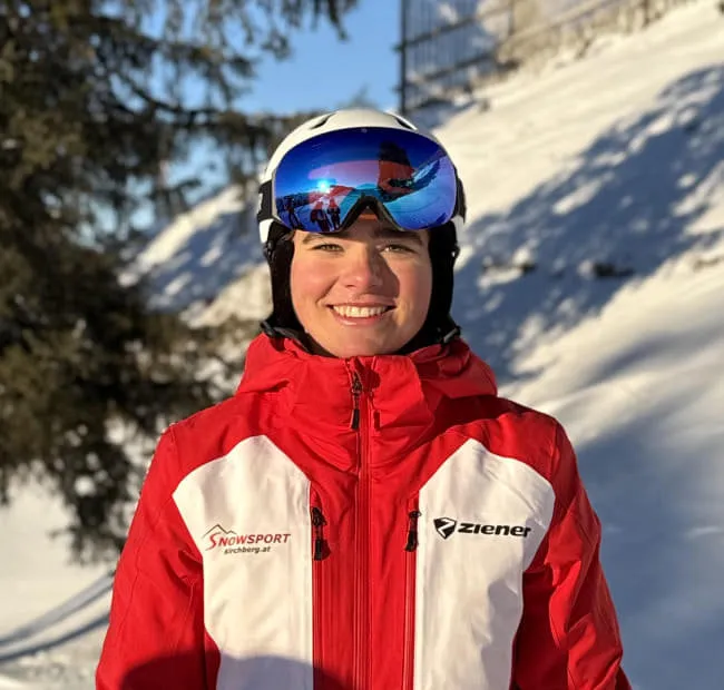 Skifahrerin in roter Jacke mit Skibrille im Schnee.