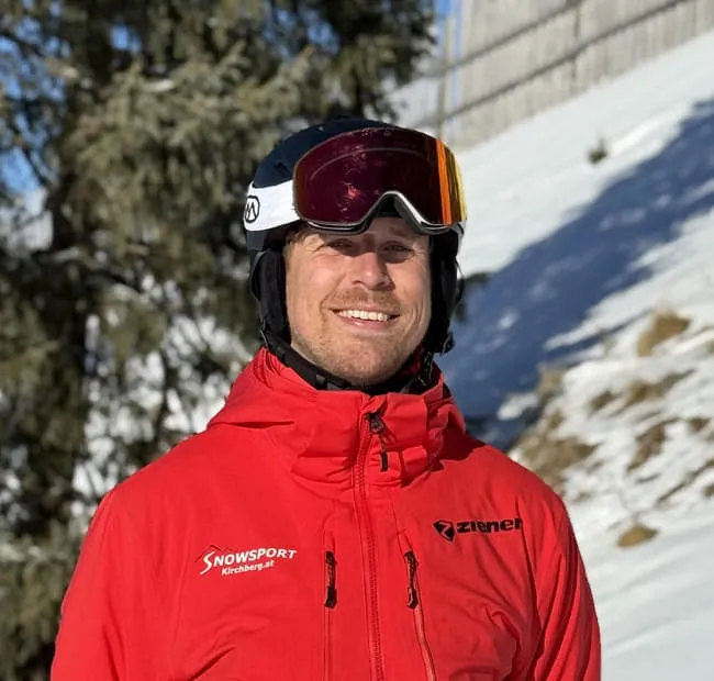 Lächelnder Skifahrer in roter Jacke auf verschneitem Hang