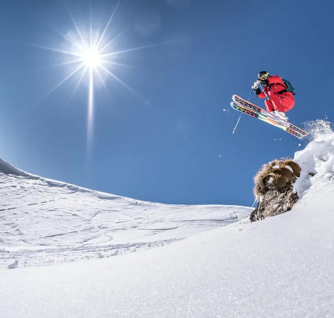 Skifahrer springt über Schnee mit heller Sonne am Himmel