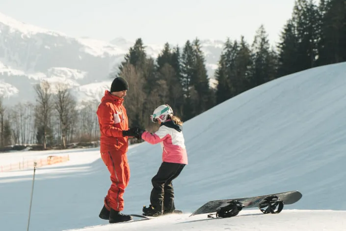 Skilehrer hilft einem Kind beim Snowboarden in Kirchberg